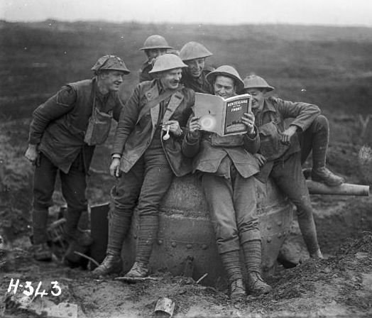 black and white photograph of 6 New Zealand soldiers crowded around a printed magazine of New Zealand at the Front. The soldiers are on the battlefield, wearing helmets and leaning against a tank turret. The photograph is dated 20 November 1917. 