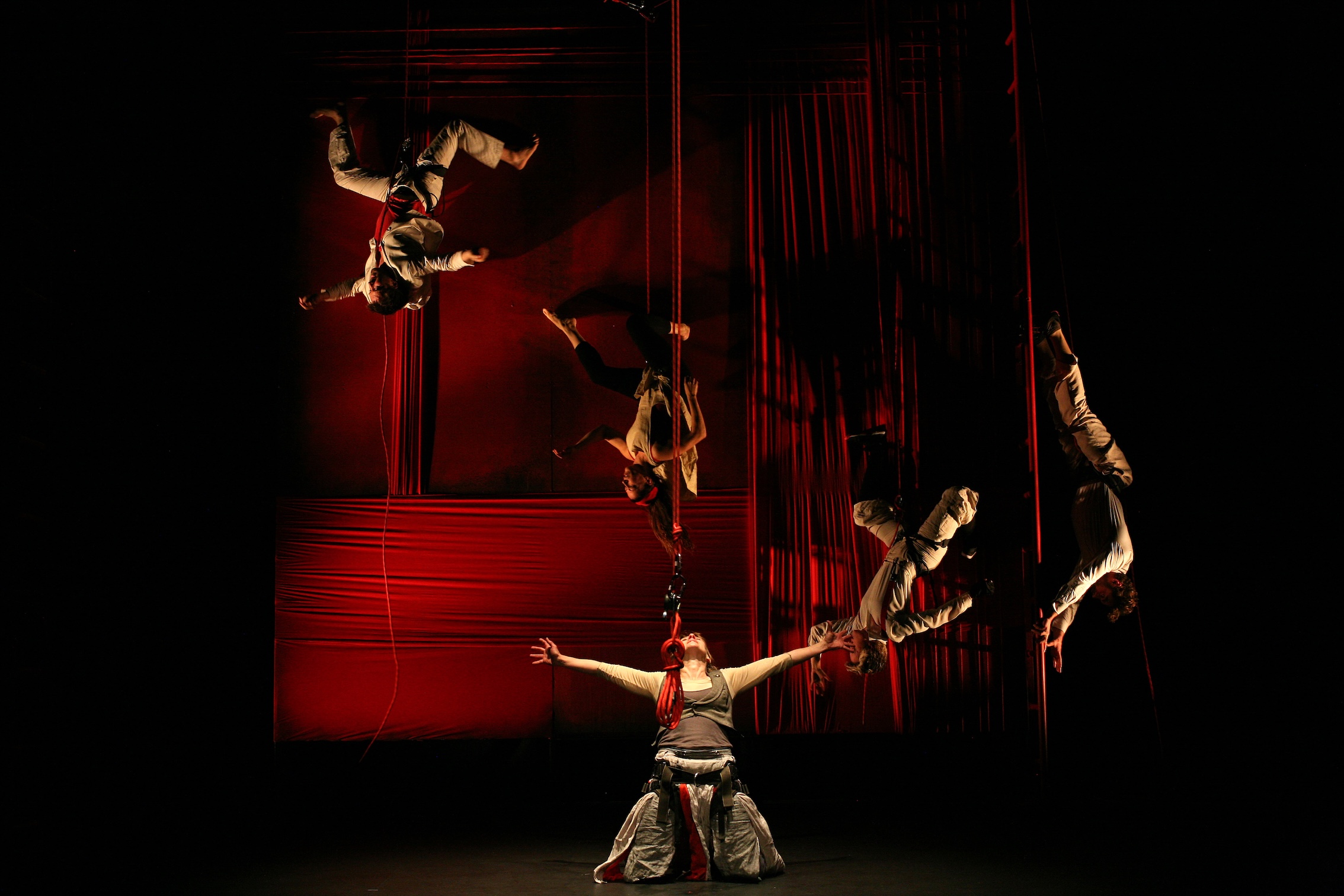A colour image of a theatrical performance: a scene from “Aerial Medea” with performers suspended in mid-air (from an aerial apparatus) above the stage