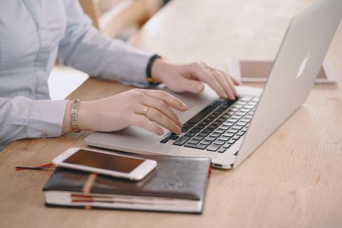 Hands on laptop keyboard with book and phone