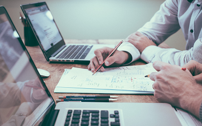 Person holding pencil over paper next to laptops - Scott Graham on Unsplash