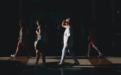 Photo shows a group of women walking along the street, they are looking ahead and one has her hand up to block the bright sunshine that is shining on her face