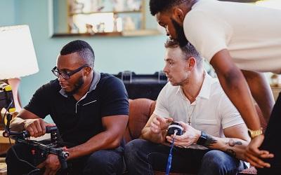Three male content producers look at a screen to see how the video they are editing looks like