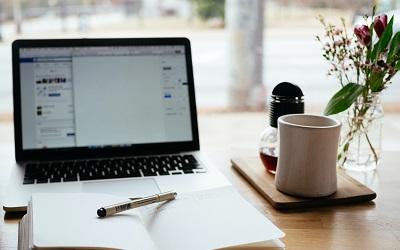 Image shows a laptop on a desk with a notepad and pen by it, along with some flowers and a cup of coffee. Photo credit Nick Morrison on Unsplash