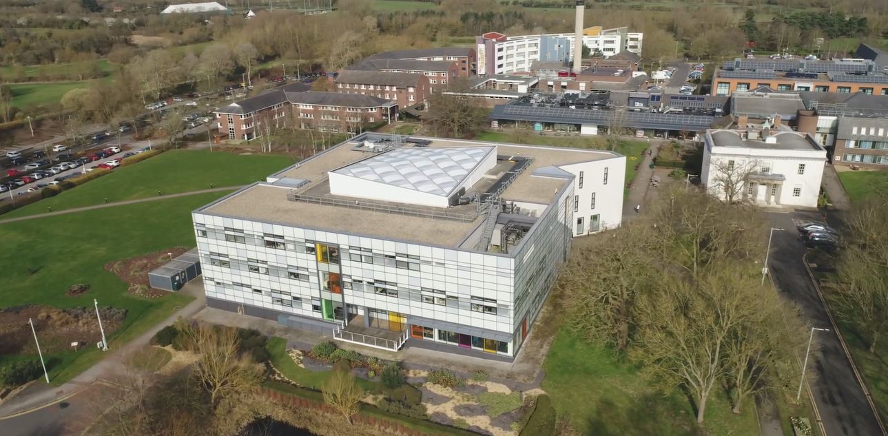 Image of building from the air. Two of the buildings show rows of Solar Photovoltaic panels. The buildings are surrounded by grass and gardens including a pond.