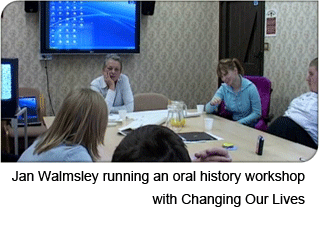 Jan Walmsley and other people sitting round tables in a room, with a digital projector screen in the background