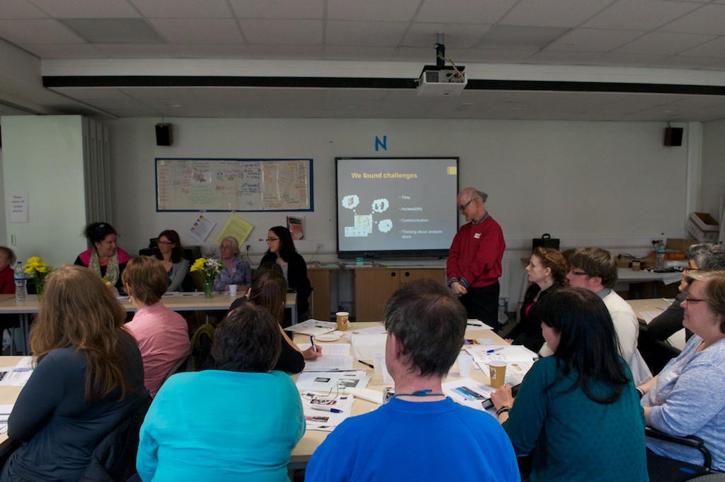 Speakers and participants sitting round tables, looking towards a person giving a presentation