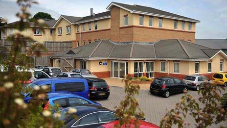 A photo of a building, with cars parked outside in a courtyard