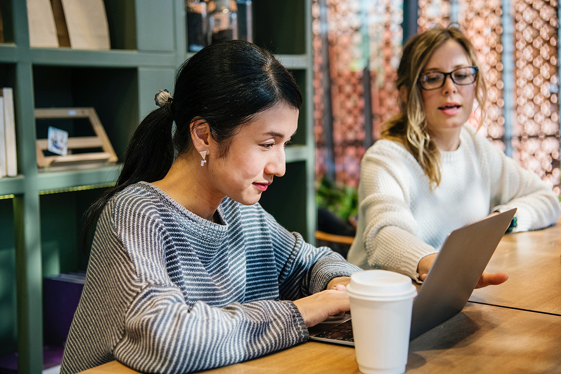 Photo of two women looking at laptop, one indicating something on screen with her hand