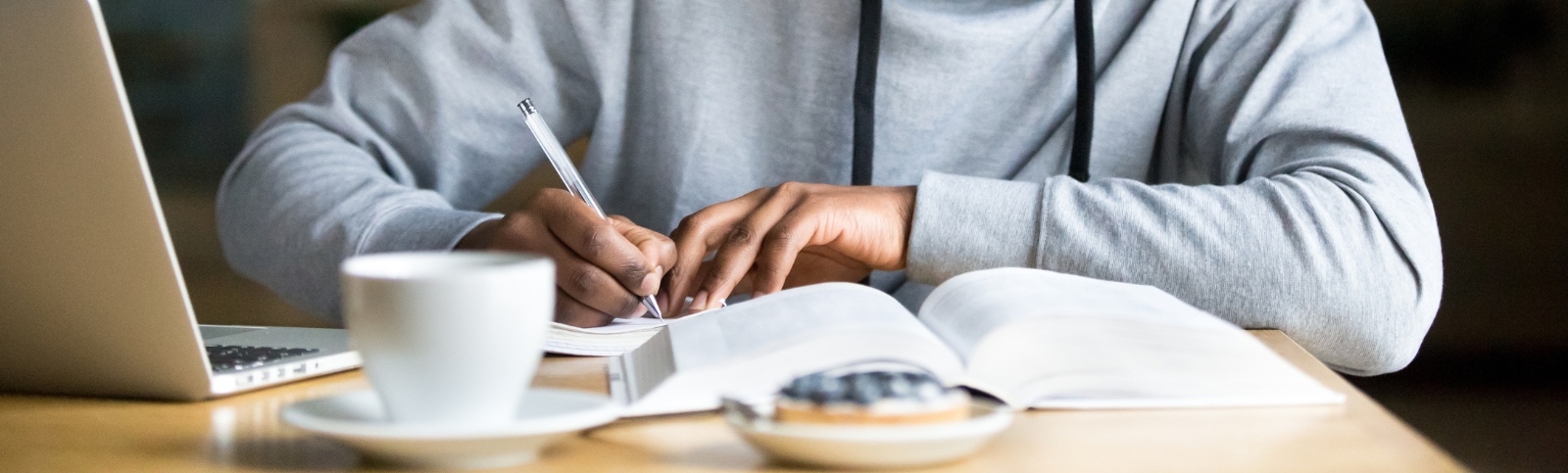 a young man writes in a notebook at a desk with a text book in front of him