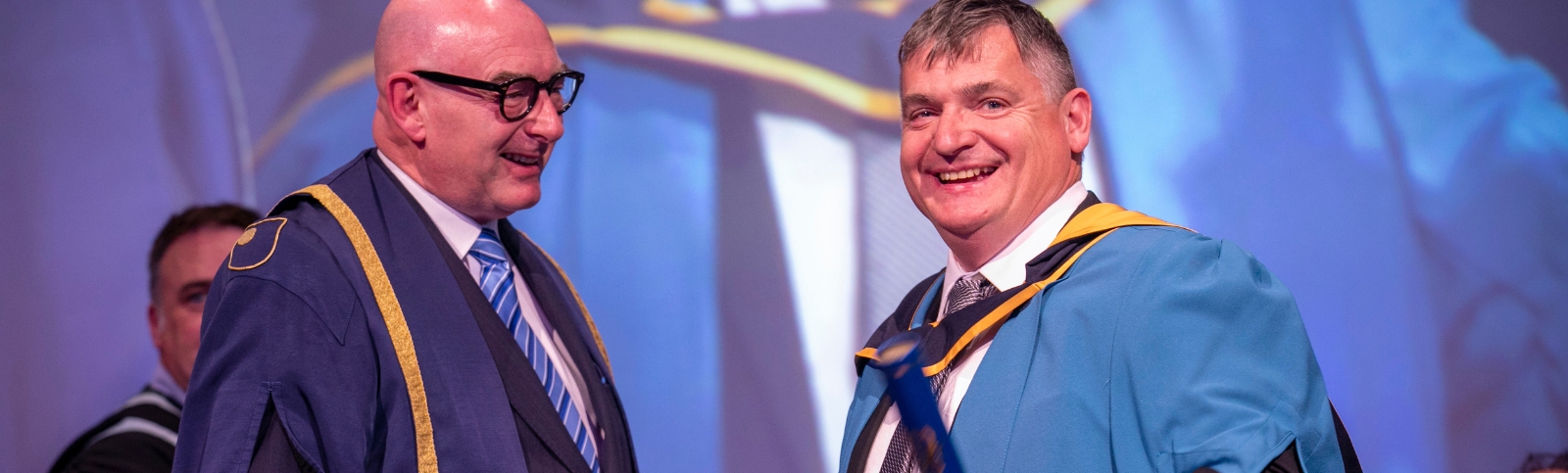 two men smile in their graduation robes