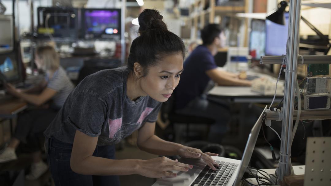 An engineering student in a workshop. She is at her workstation, looking at her screen in deep concentration.