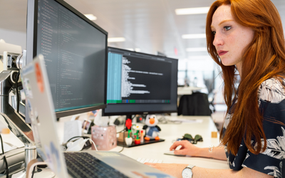 A girl in an office working at three computer screens