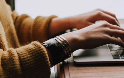 Hands typing on a laptop, the person is wearing a yellow jumper