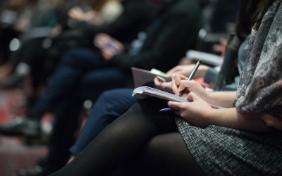 A crowd at an event writing notes in a notebook