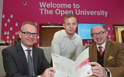 three men pose for a photo and two hold a prospectus between them