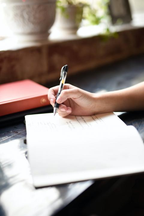 Someone writing notes in a notebook at a desk outside