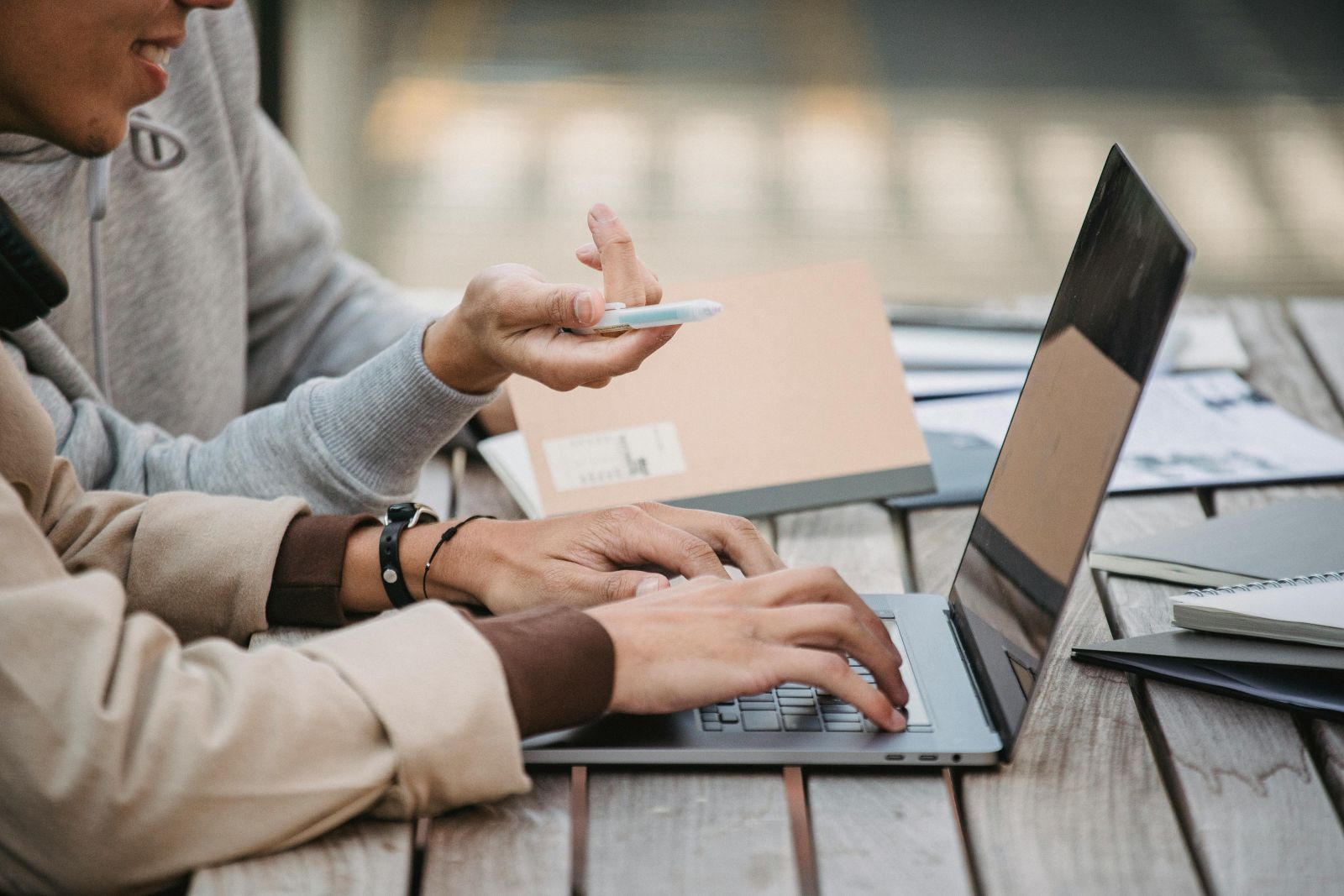 A close-up of a couple of people using a computer sitting on an outdoors bench. Photo by Armin Rimoldi.