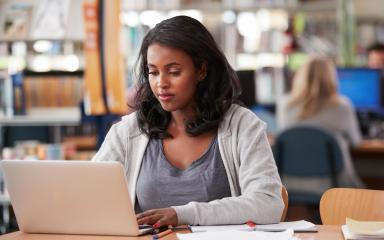 A student is sitting at a desk in a Library, looking at an open laptop