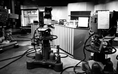 Black and white photo of a vintage television studio with large cameras on wheeled pedestals facing a news desk.