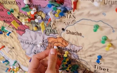 Hand placing a pin on a colourful map of South Asia.