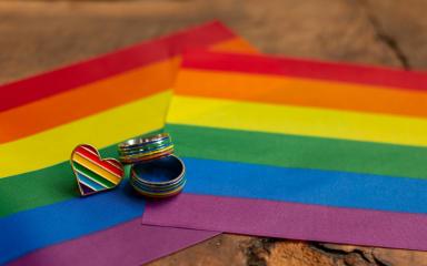 Two Pride flags are displayed on a table top, underneath a Pride heart-shaped badge and two rings.