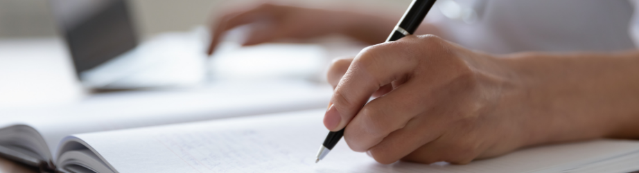 Student writing in a journal and searching on a laptop