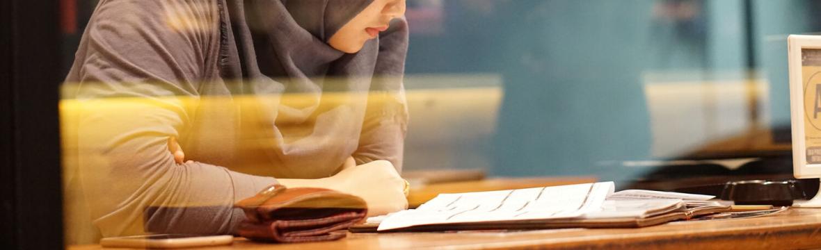 Student wearing a head covering, studying in a cafe