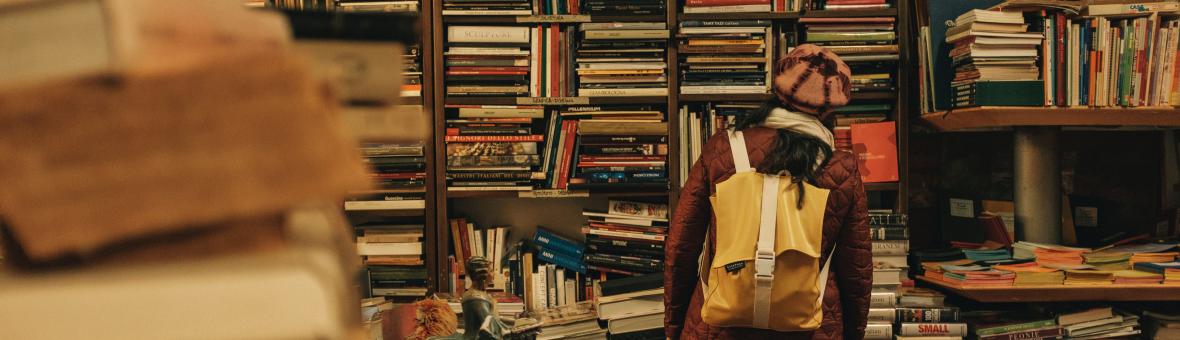 Young female student looking at books in book shop and surrounded by lots of books