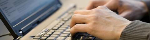 Image focusing on hands using a laptop keyboard.