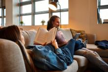 Couple relaxing on a couch in a sunlit room, one reading a book while the other uses a tablet.