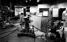 Black and white photo of a vintage television studio with large cameras on wheeled pedestals facing a news desk.