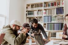 Group of students sharing and enjoying studying whilst looking at a laptop, with book shelves in the background