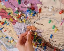 Hand placing a pin on a colourful map of South Asia.