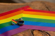 Two Pride flags are displayed on a table top, underneath a Pride heart-shaped badge and two rings.