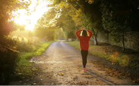 a woman walking on a forest path as the sun starts to break