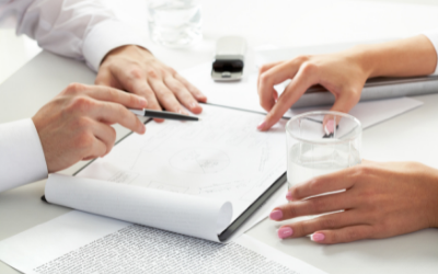 a picture of hands around a piece of paper on a desk as people discuss it