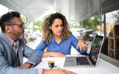 a man and a woman sit at a laptop and discuss what is on the screen