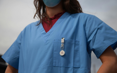 The torso of a woman in a blue nursing uniform looking towards the camera, her face is not visible