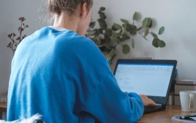 A female in a blue jumper looking at a laptop whilst seated at a desk