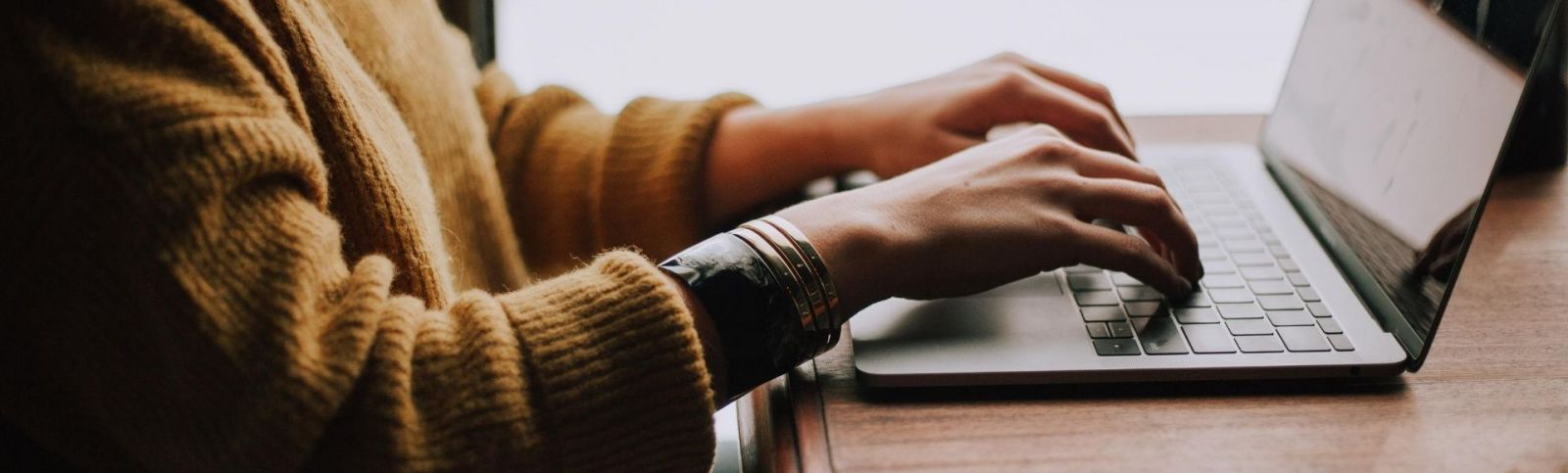 someone with a mustard woolly jumper typing on a laptop