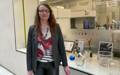 Tanya stood in front of awards an certificates outside a lab