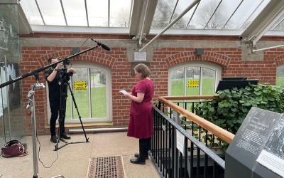 A woman stands in front of a camera reading a script