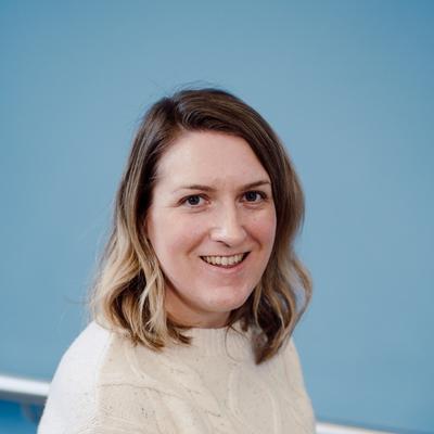 A picture of Christine Murphy who has fair curly hair and is smiling and wearing a white jumper