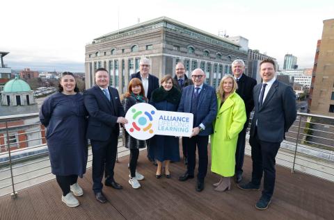 a group of people stand posing for a photo, one is holding a board which say Alliance for Lifelong learning