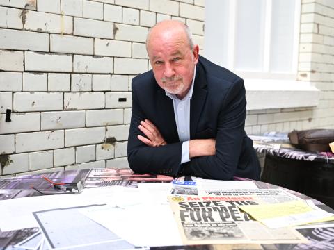 A man in a suit leaning over a table looking at old newspaper clippings