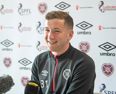 a young man wearing a football top smiles whilst being interviewed by media