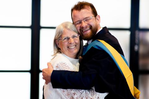 Colm, dressed in OU graduation robes, hugging his mum.