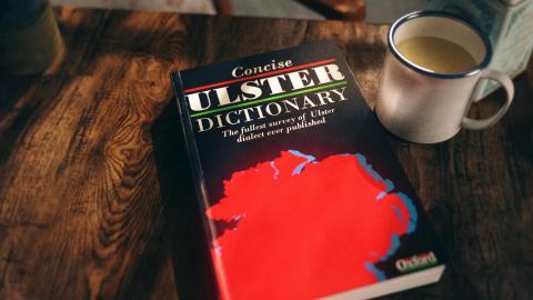 a concise ulster dictionary sits on a table with a cup beside it