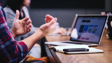 an image if a man sitting at desk moving his hands in front of a laptop and notebook