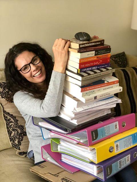 A woman holds a pile of books on her knee right up to her head